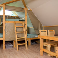 Inside an oTENTik accommodation, there is a sleeping area separated by curtains, a kitchen table and chairs, and a place to prepare meals and store equipment.