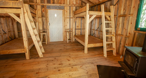 Two sets of wooden bunk beds and a wood stove inside a rustic cabin.