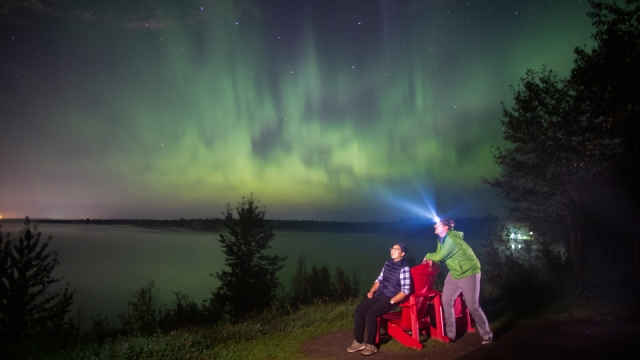 A couple watching the Northern lights from a set of red chairs.