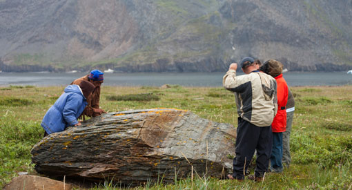 Visitors inspect a large rock on the shore of the river.