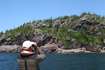 Using binoculars, a man observes a rocky shoreline.