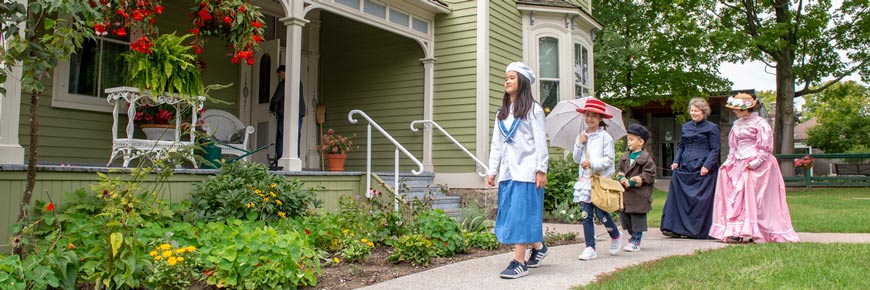A guide and visitors in period costumes walking in front of the Victorian home at the Bethune Memorial House National Historic Site.