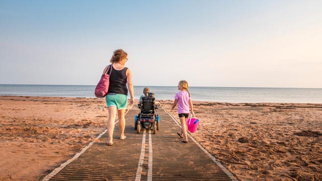 A family with accessibility needs walks to the water at Stanhope Beach using mobility mats