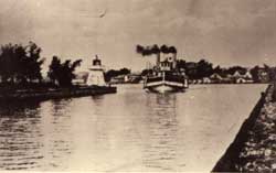 Steamboat entering the Becker dam. To the left, a small lighthouse. In the background, the town of Sainte-Anne-de-Bellevue, 1910.